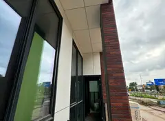 Gevel met grote ramen en lichte panelen onder de overkapping.