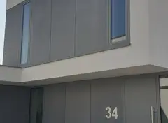 Huis met gladde grijze gevel en nummer 34 op de muur.