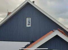 Dak van een huis met blauwe houten gevel en witte omlijstingen.
