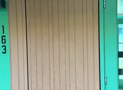 Close-up van een geveldeel met verticale bruine panelen en turquoise deur met het nummer 163.