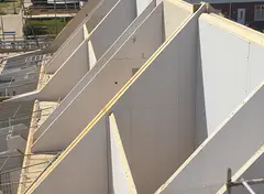 Schuine prefabwanden die de dakvorm vormen van een gebouw in aanbouw.