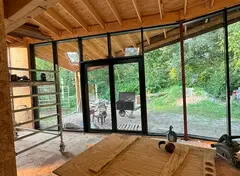 Huis in aanbouw met houten plafond, werkbank en grote glazen schuifdeuren met uitzicht op de tuin.