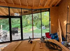 Interieur van een houten constructie met werktafel, gereedschap en grote ramen met uitzicht op het groen.