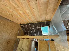 Schuin houten plafond met isolatie en gedeeltelijk aangebrachte dampremmende folie, ladder en dakraam zichtbaar.