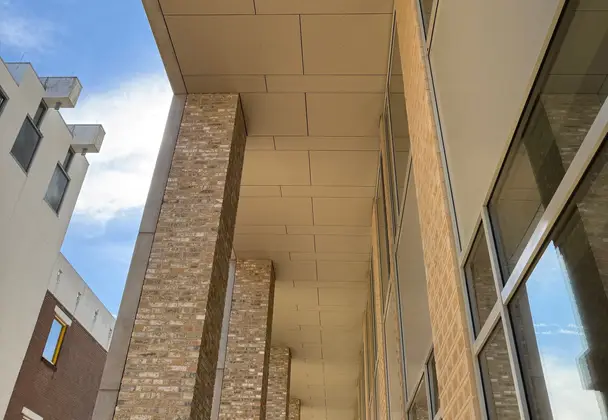 Kolonnade van lichte baksteen en plafond van gevelpanelen bij een modern gebouw.