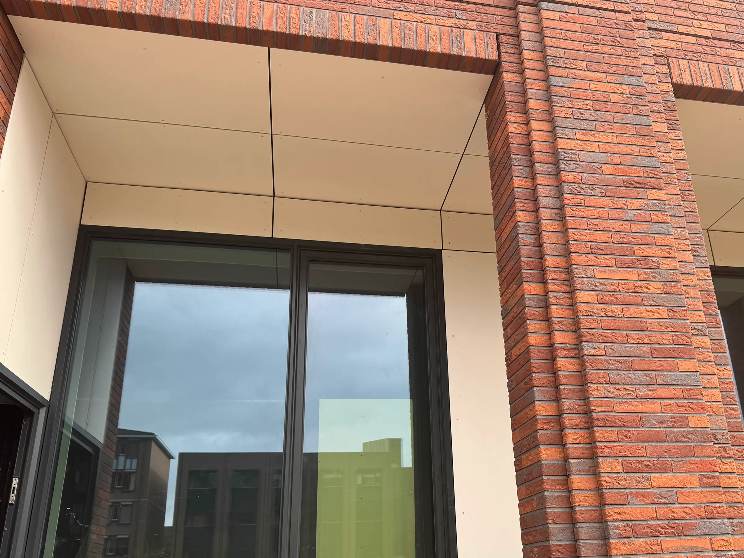 Fragment van een gevel met rode baksteen en lichte plafondpanelen.