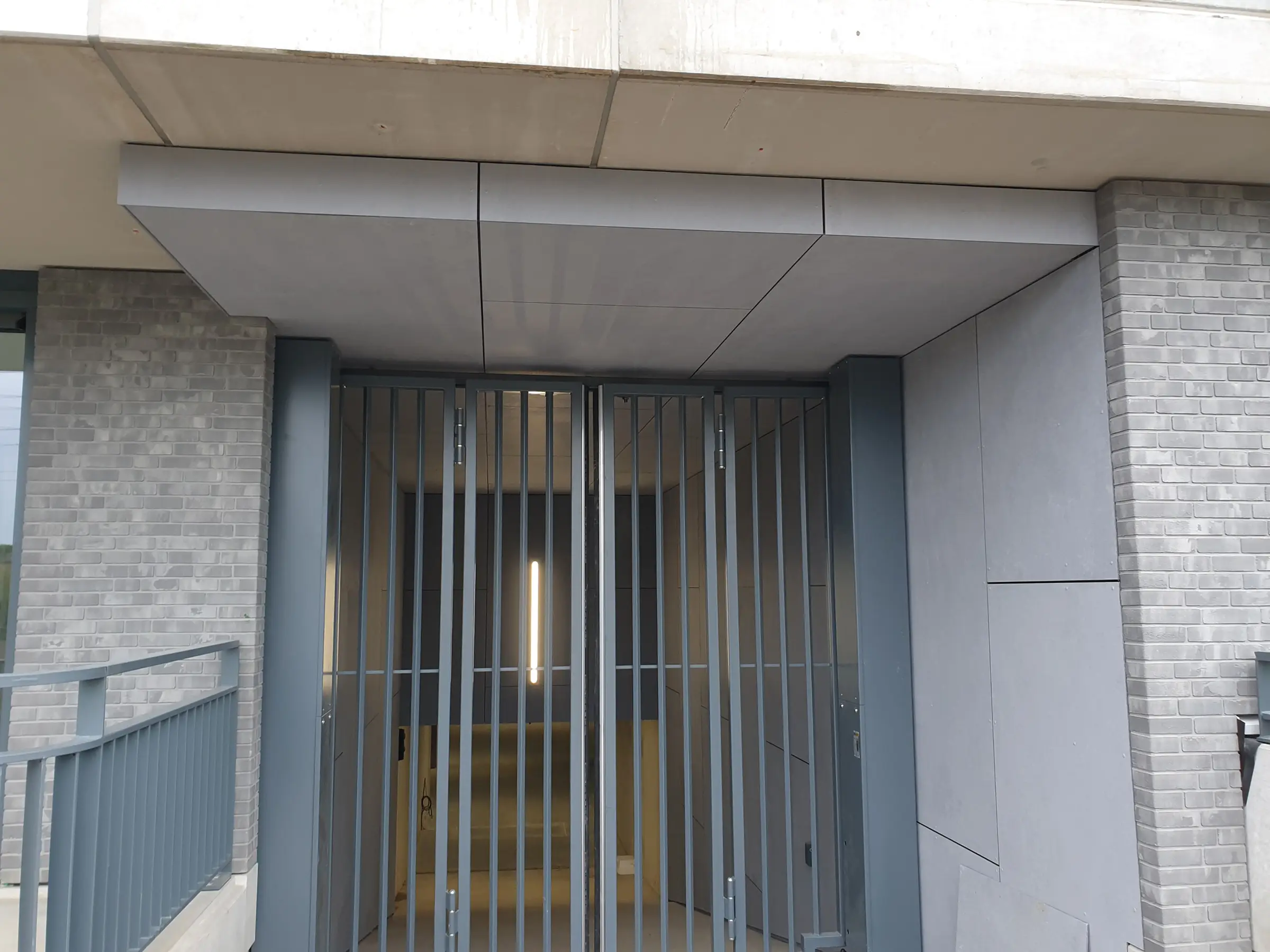 Ingang met metalen poort en bekleding van grijze platen.