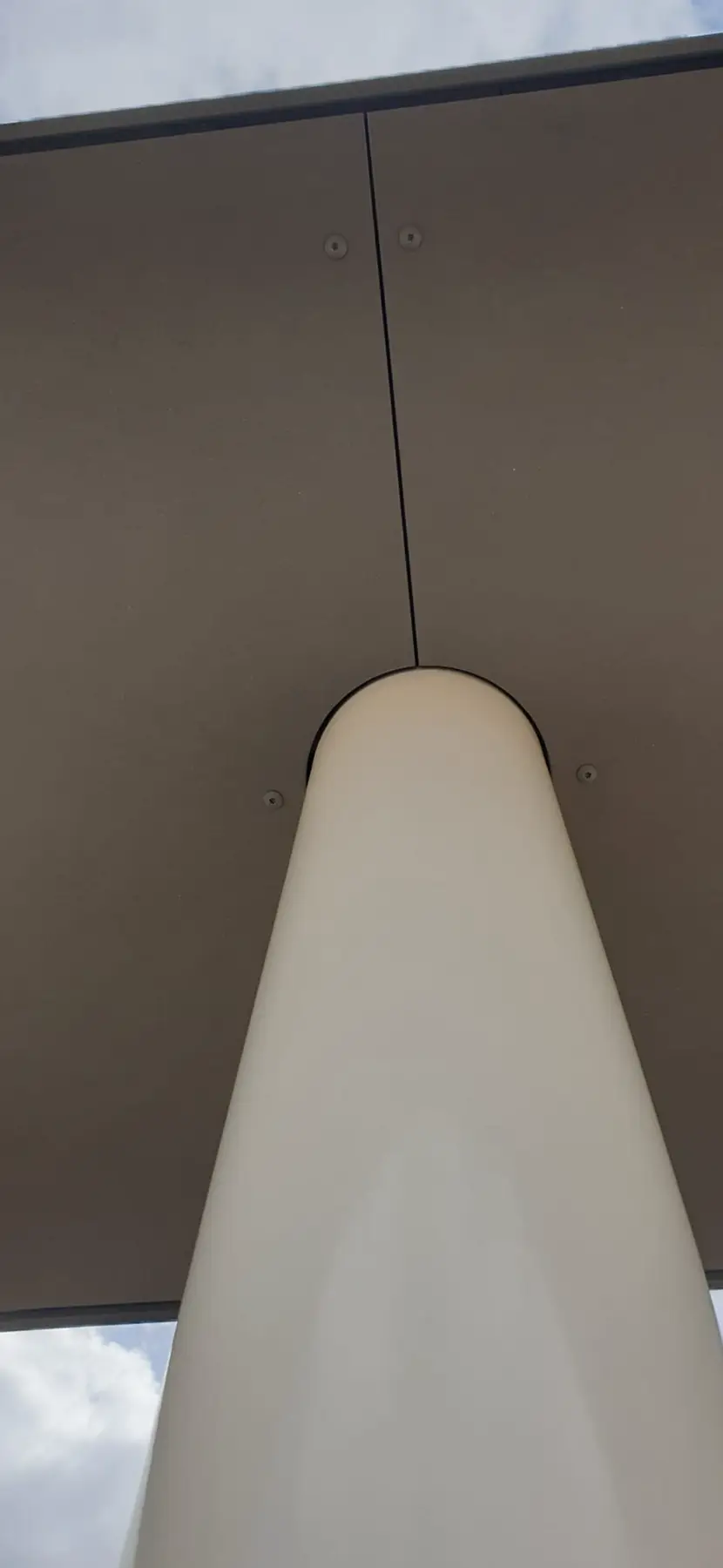 Kolom die een plafond van donkere gevelpanelen ondersteunt.