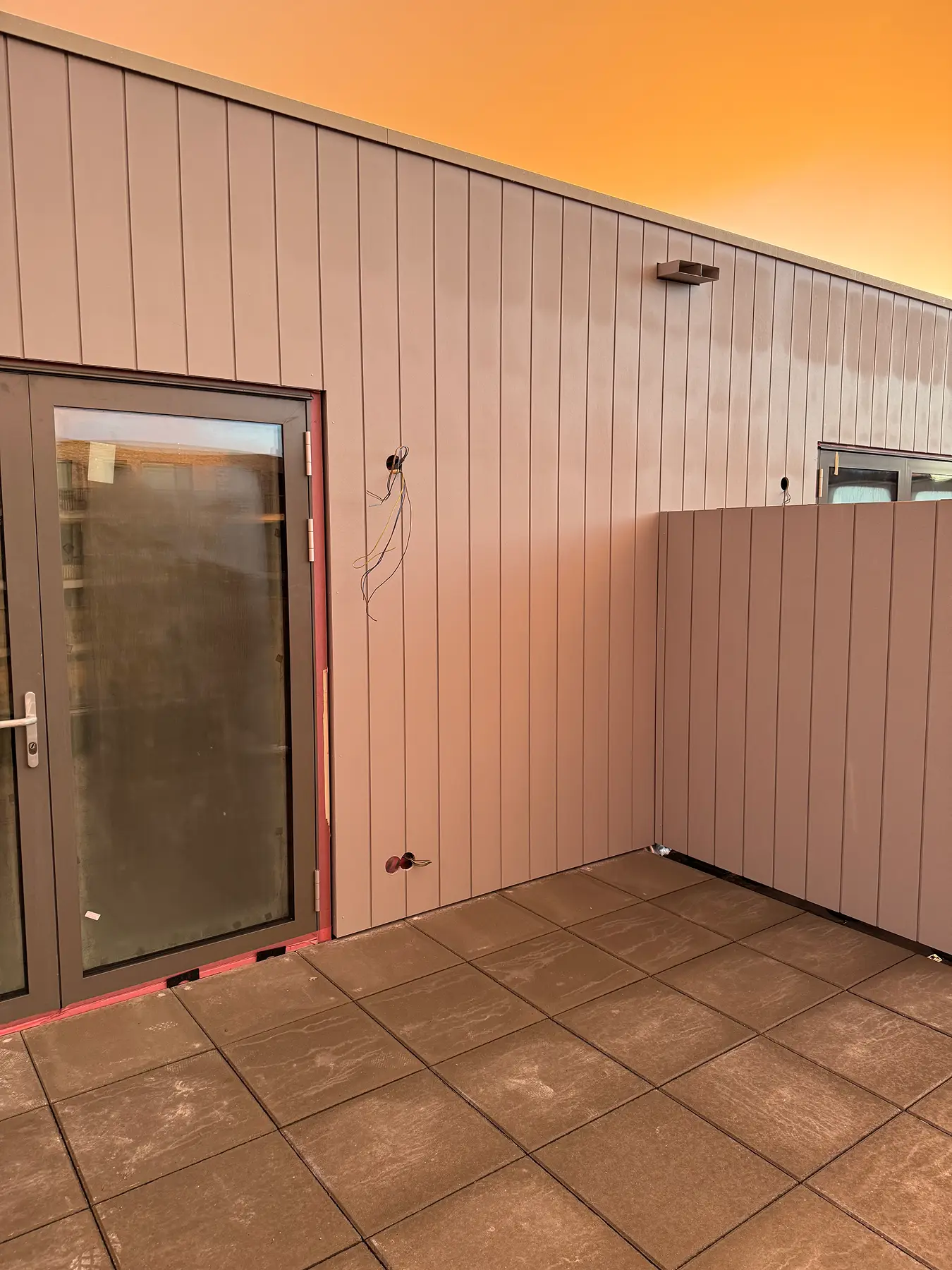 Muur van verticale composietpanelen bij terras en balkondeuren.