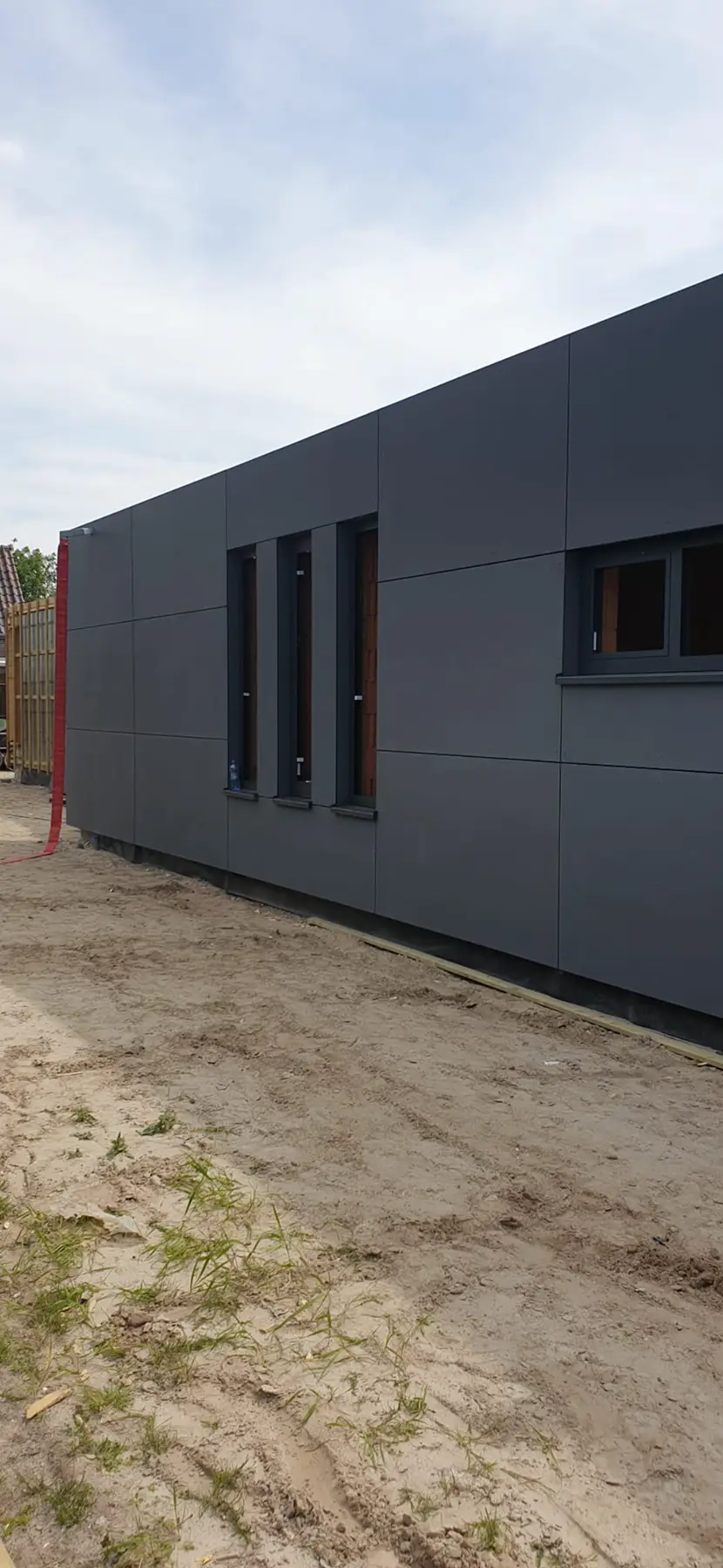 Laag gebouw met donkere grijze gevel van grote panelen.