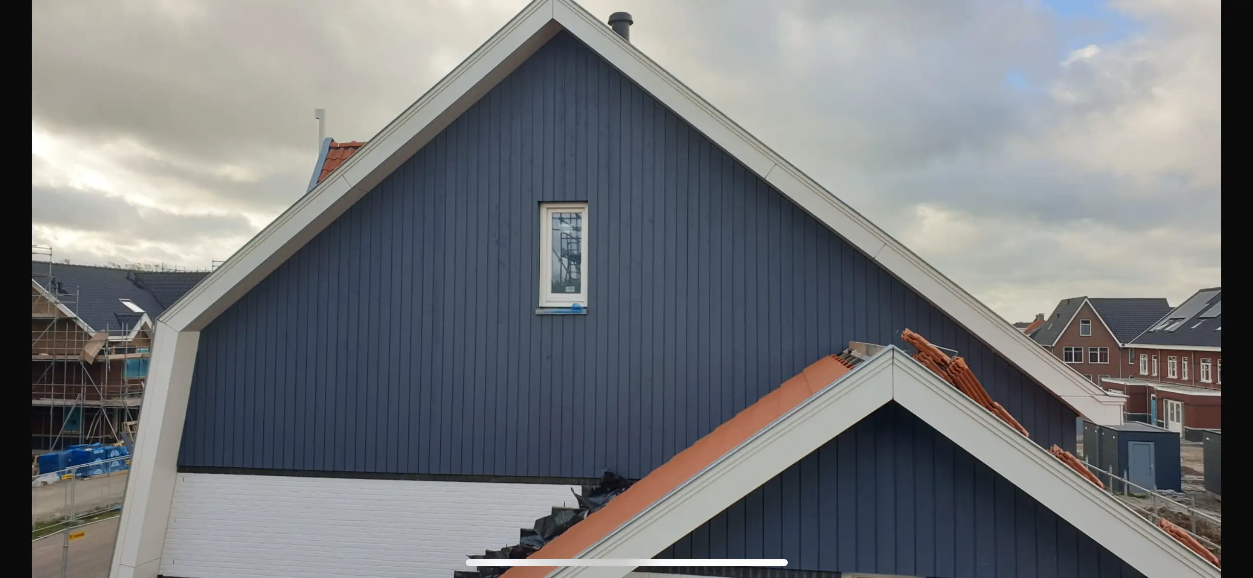 Dak van een huis met blauwe houten gevel en witte omlijstingen.