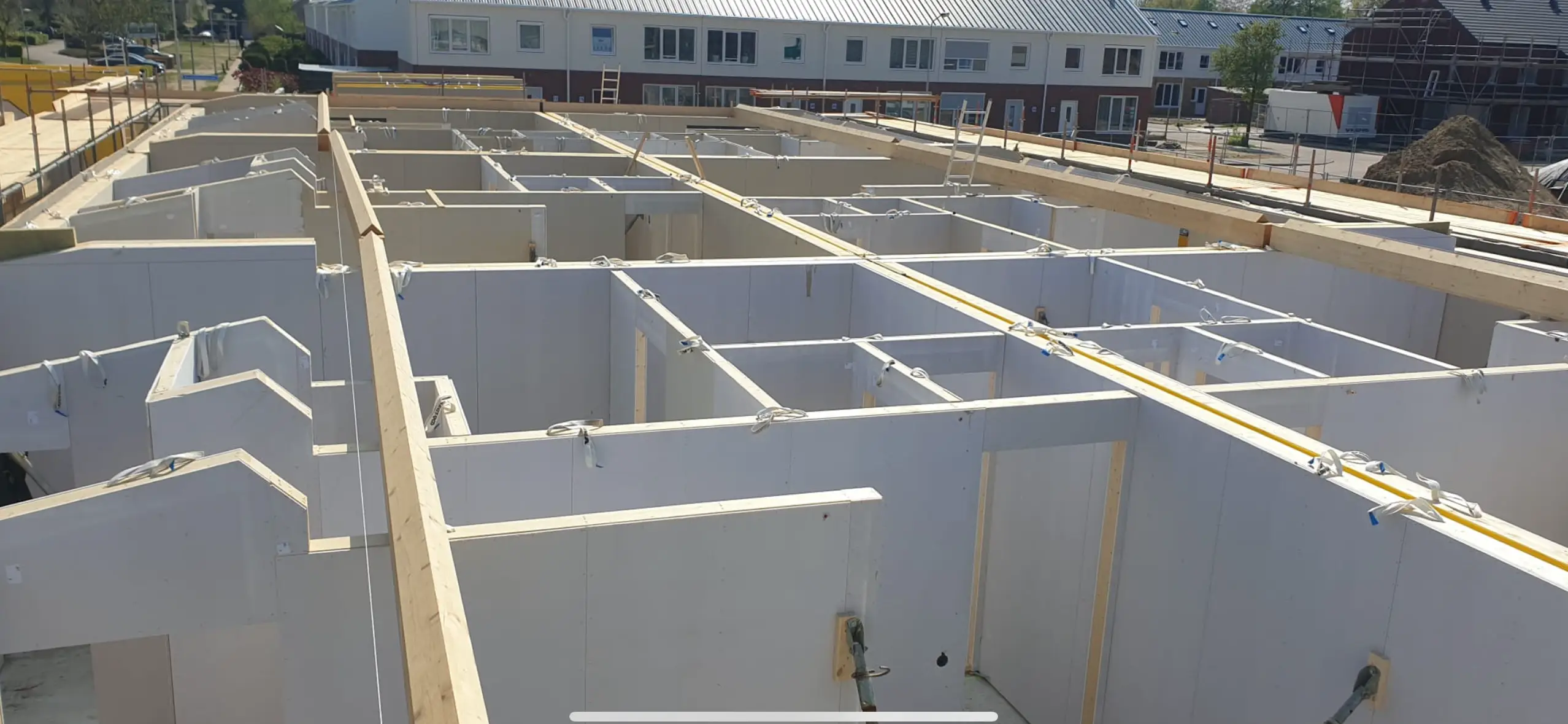 Bouwconstructie in montagefase met witte prefabwanden en houten draagbalken.