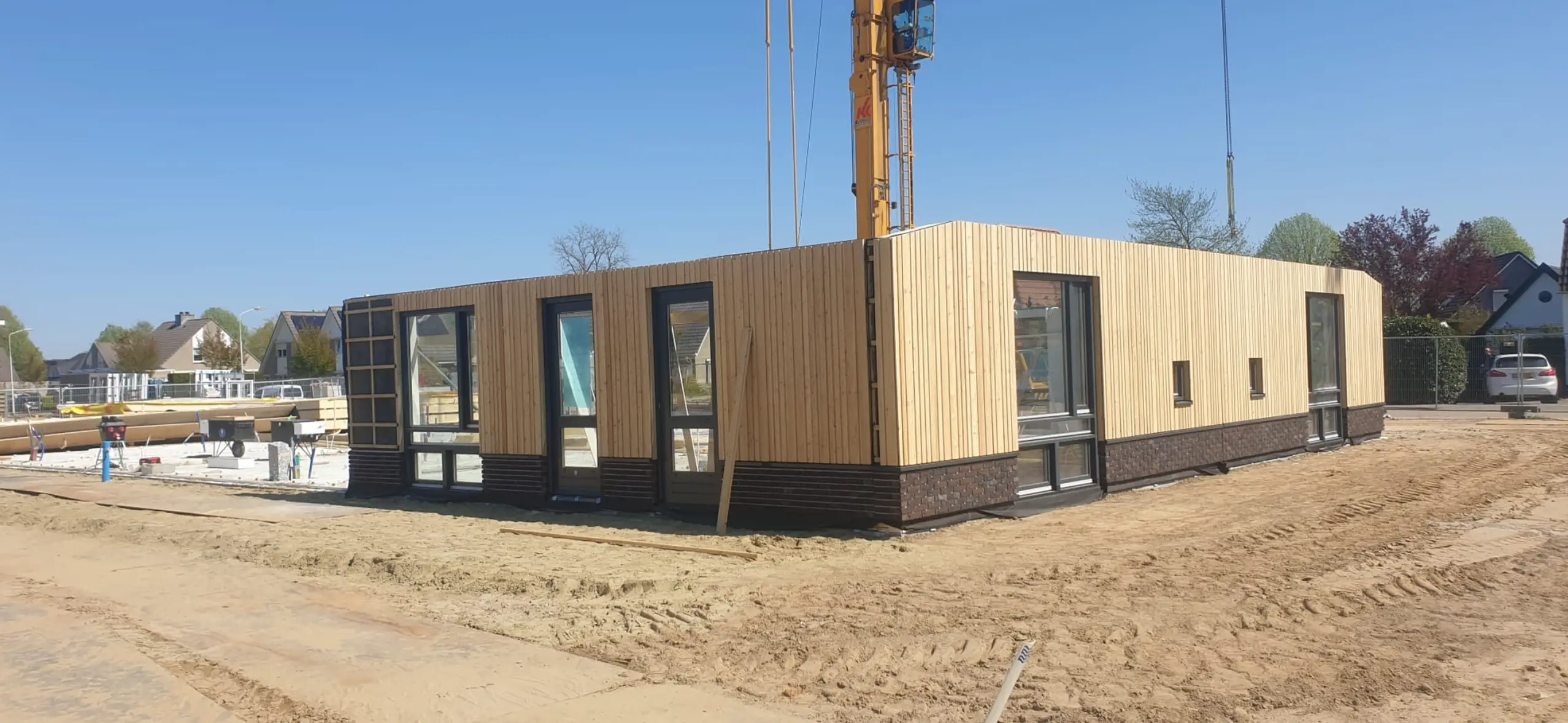 Huis in aanbouw met gevel van verticale houten latten en grote ramen.