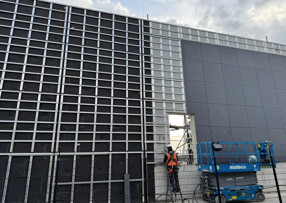 Montage van een geventileerde gevel; een werknemer op een hoogwerker bevestigt gevelpanelen.